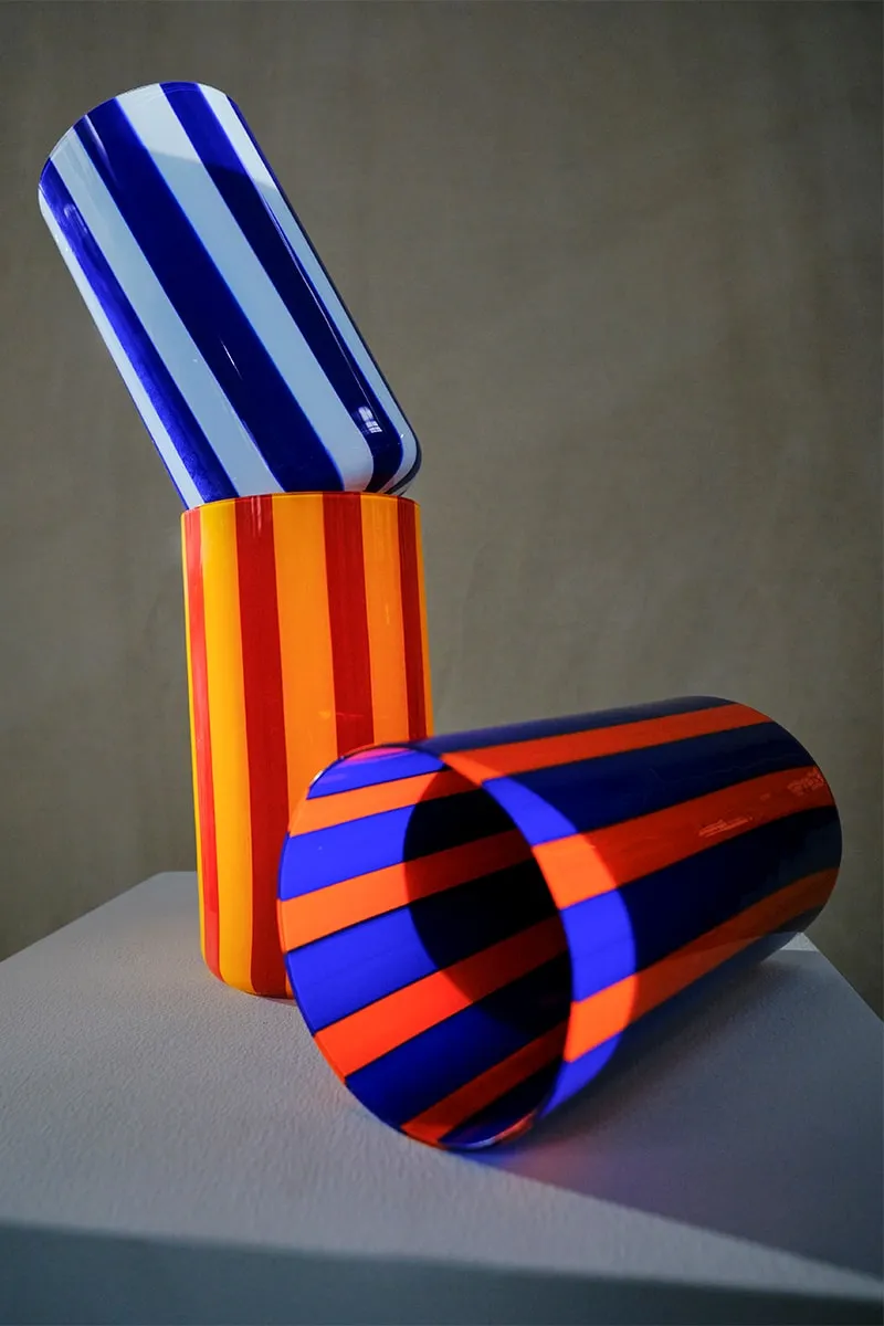 Deux vases aux rayures colorées, un bleu et blanc, l'autre orange et rouge, sur un socle.