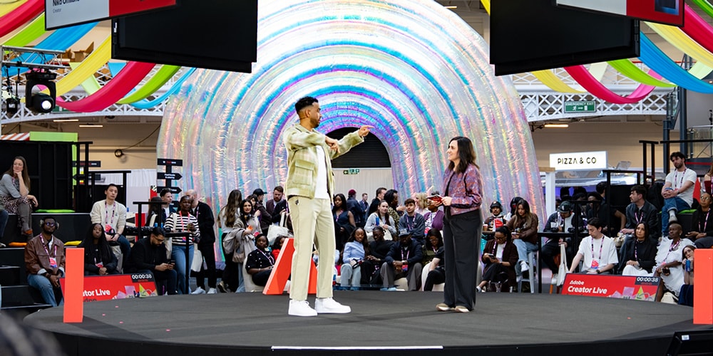 Deux personnes sur scène devant un public, décor coloré en arrière-plan.