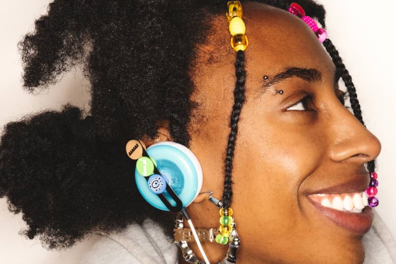 Personne avec écouteurs colorés et perles dans les cheveux souriant.