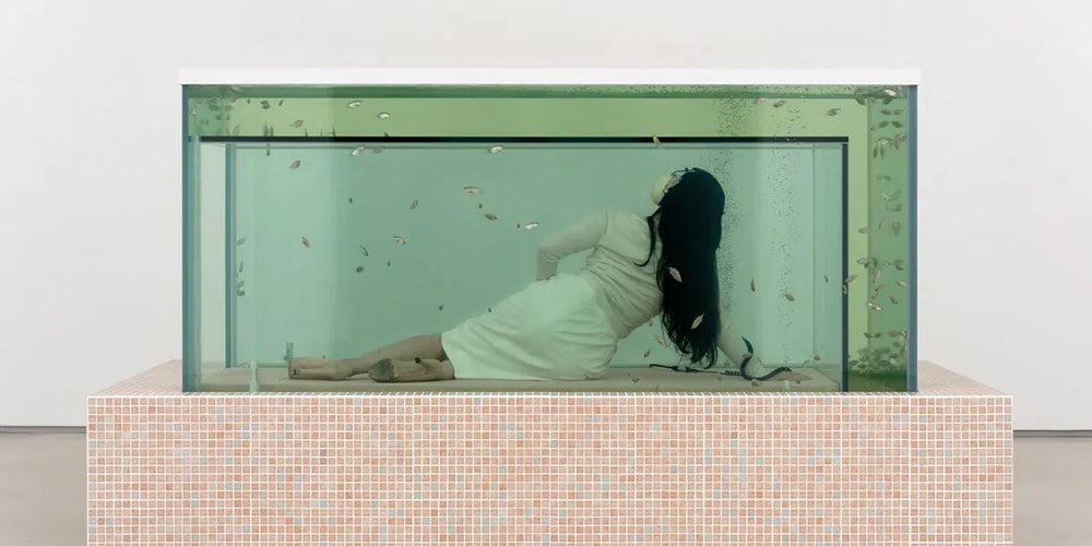 Femme allongée dans un grand aquarium avec des poissons nageant autour.