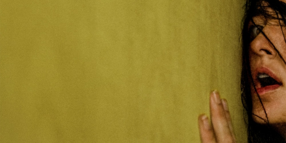 Visage partiellement visible d'une personne avec cheveux sombres contre un mur jaune.