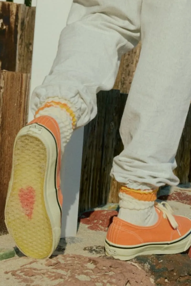 Chaussures orange avec cœur rouge sous la semelle, bas blancs et pantalon clair.