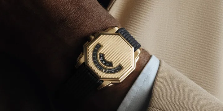 Montre dorée hexagonale sur poignet avec costume beige.