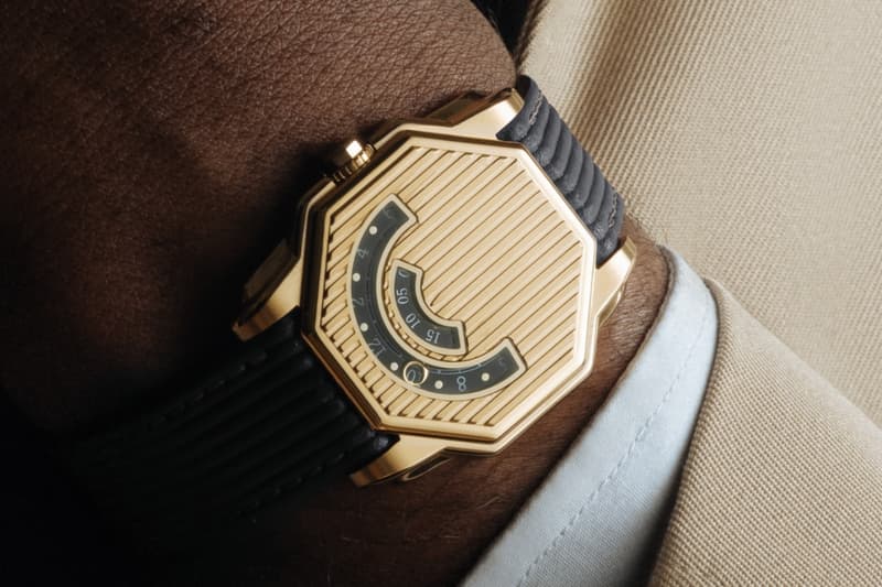 Montre dorée hexagonale avec bracelet noir sur poignet habillé.