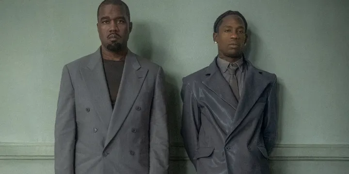 Deux hommes en costumes gris devant un fond vert.