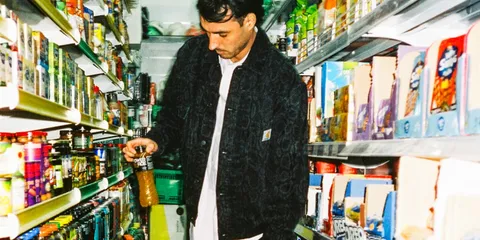 Homme dans une épicerie, tenant une bouteille sur l'étagère.