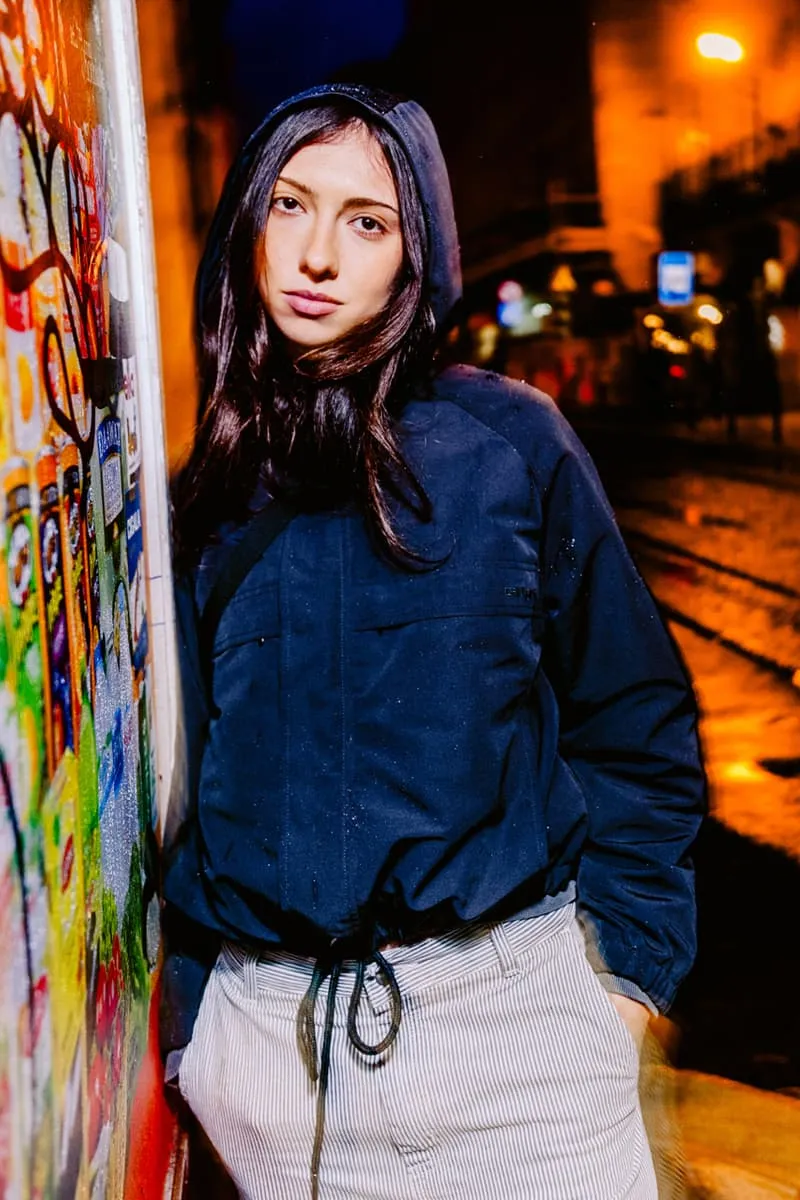 Femme en manteau à capuche posant devant un mur coloré la nuit.