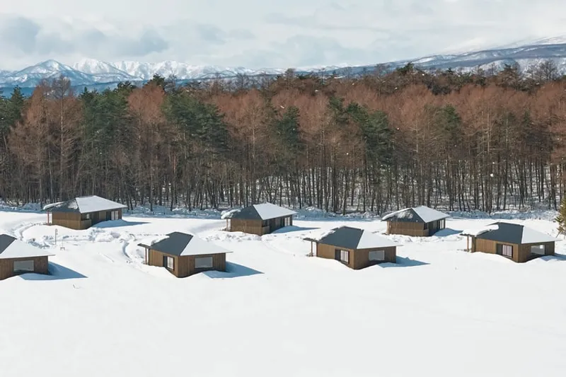 Cabanes en bois dans la neige avec une forêt et montagnes en arrière-plan.