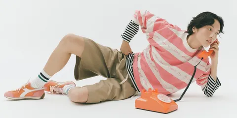 Personne posant avec un téléphone orange, tenue décontractée et colorée.