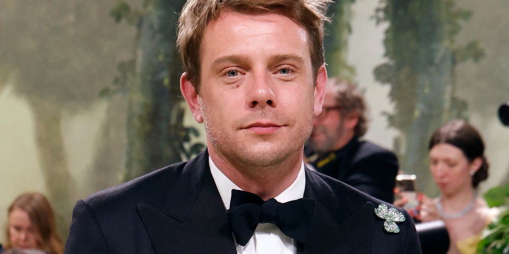 Homme en costume noir avec noeud papillon et broche, arrière-plan flou