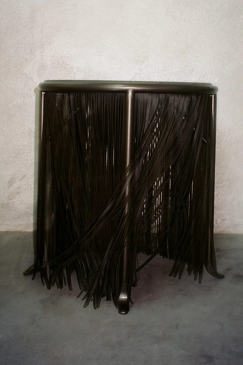 Tabouret moderne avec franges noires suspendues, ambiance minimaliste.