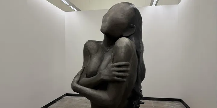 Sculpture sans visage, bras croisés, dans une galerie.