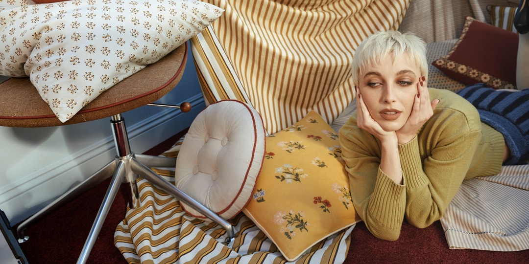 Personne allongée sur un tapis avec oreillers et tissu rayé autour.