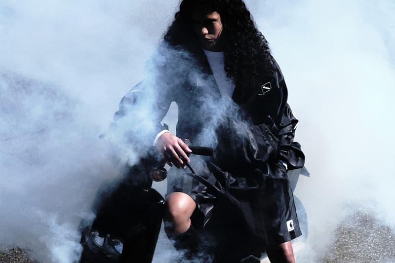 Personne avec long manteau noir et cheveux bouclés entourée de fumée.