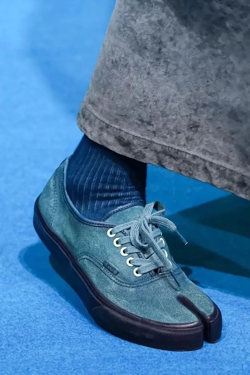 Chaussure bleu avec semelle noire et chaussette rayée sur fond bleu.