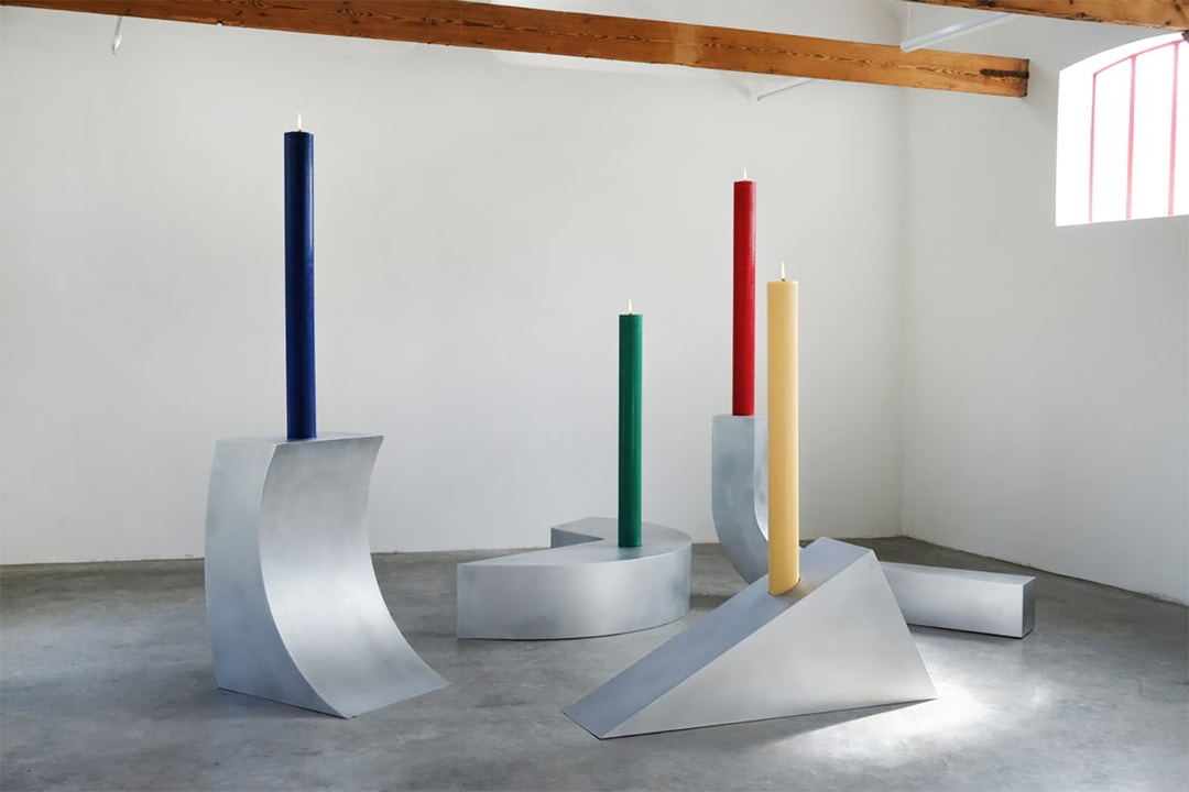 Quatre bougies colorées sur des structures métalliques géométriques dans une salle.