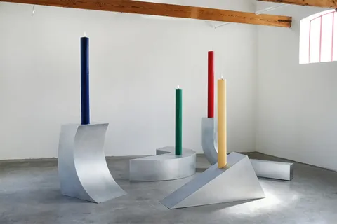 Quatre bougies colorées sur des structures métalliques géométriques dans une salle.