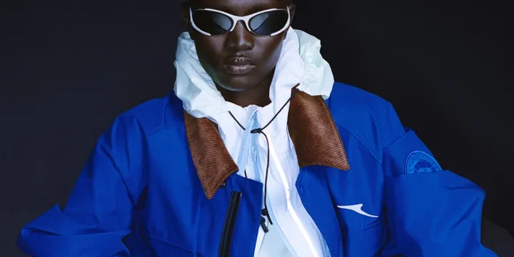 Personne portant des lunettes et une veste bleue sur fond sombre.