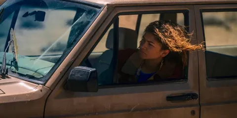 Femme conduisant une voiture marron dans un paysage désertique.