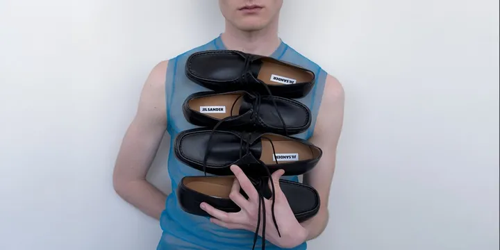 Personne tenant des chaussures noires avec étiquettes visibles 'Jil Sander'.