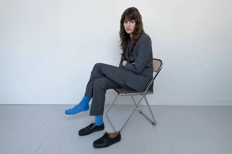 Personne en costume gris et chaussettes bleues, assise sur une chaise pliante.