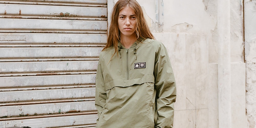 Personne portant un coupe-vent vert devant un mur industriel.