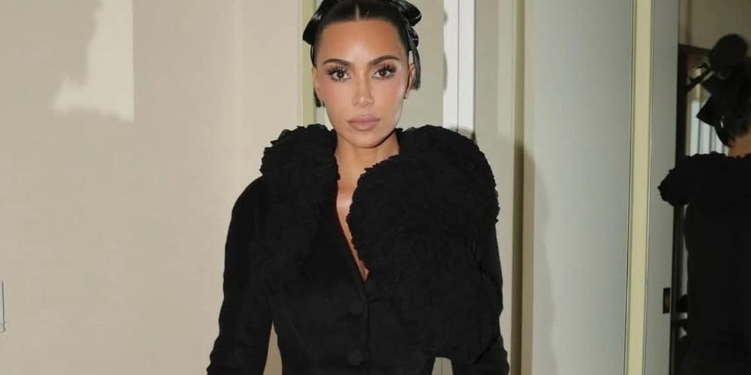 Femme en tenue noire élégante, cheveux relevés, sur fond de miroir.