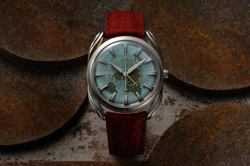 Montre avec cadran bleu-vert et bracelet rouge sur fond texturé rouillé.