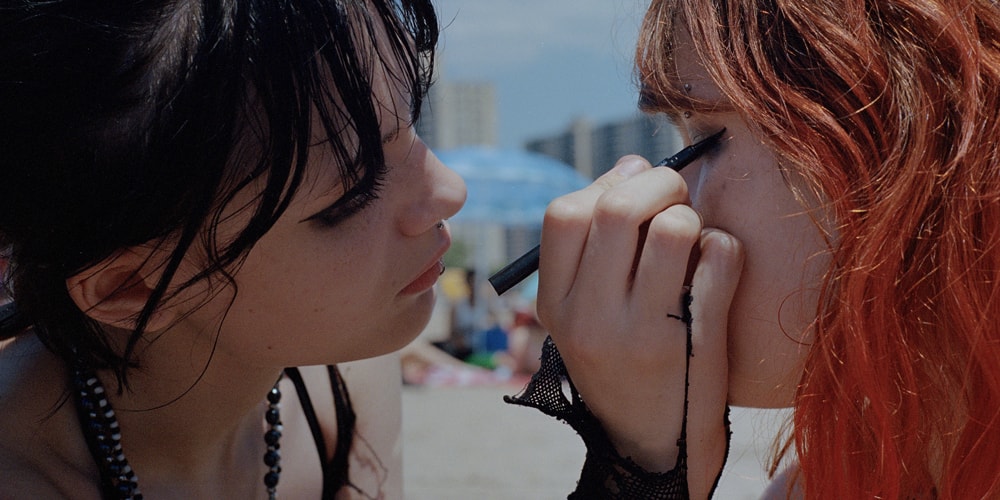 Deux personnes, l'une maquille l'autre sur une plage ensoleillée.