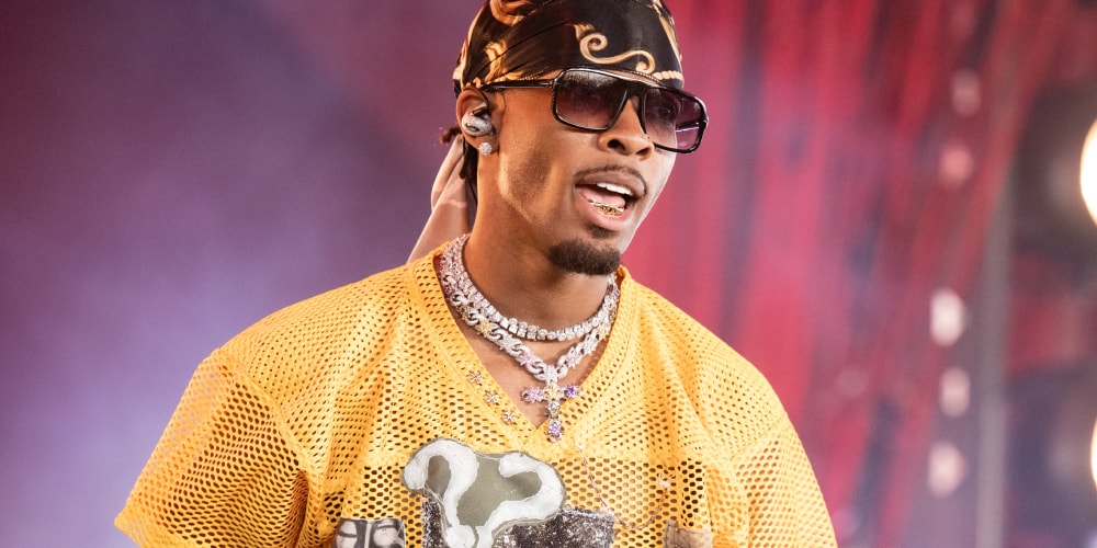 Homme en lunettes de soleil et bandana chantant sur scène.