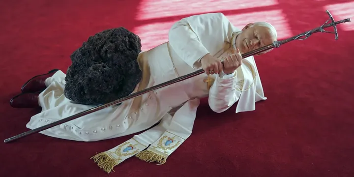 Une figure en robe blanche allongée avec un bâton et une pierre noire.