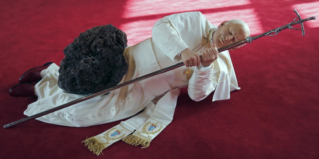 Une figure en robe blanche allongée avec un bâton et une pierre noire.