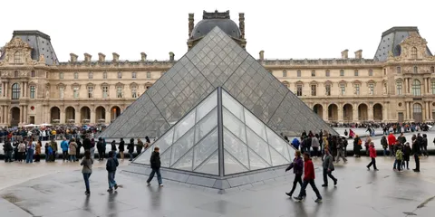 Pyramide du Louvre avec des visiteurs autour, bâtiment historique en arrière-plan.