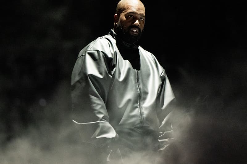 Homme en tenue sombre avec éclairage dramatique et fumée autour.