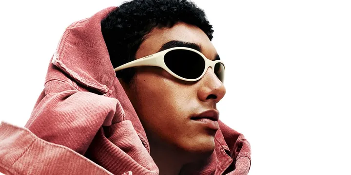 Homme avec lunettes de soleil et veste rose sur fond blanc.