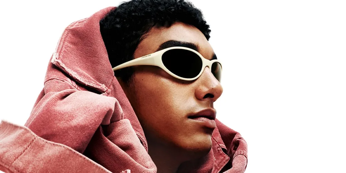 Homme avec lunettes de soleil et veste rose sur fond blanc.