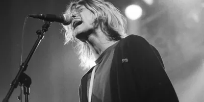 Musicien chantant sur scène avec intensité, cheveux blonds et guitare.