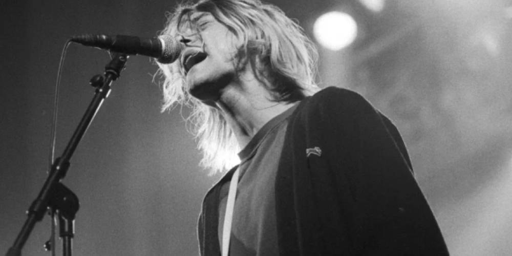 Musicien chantant sur scène avec intensité, cheveux blonds et guitare.