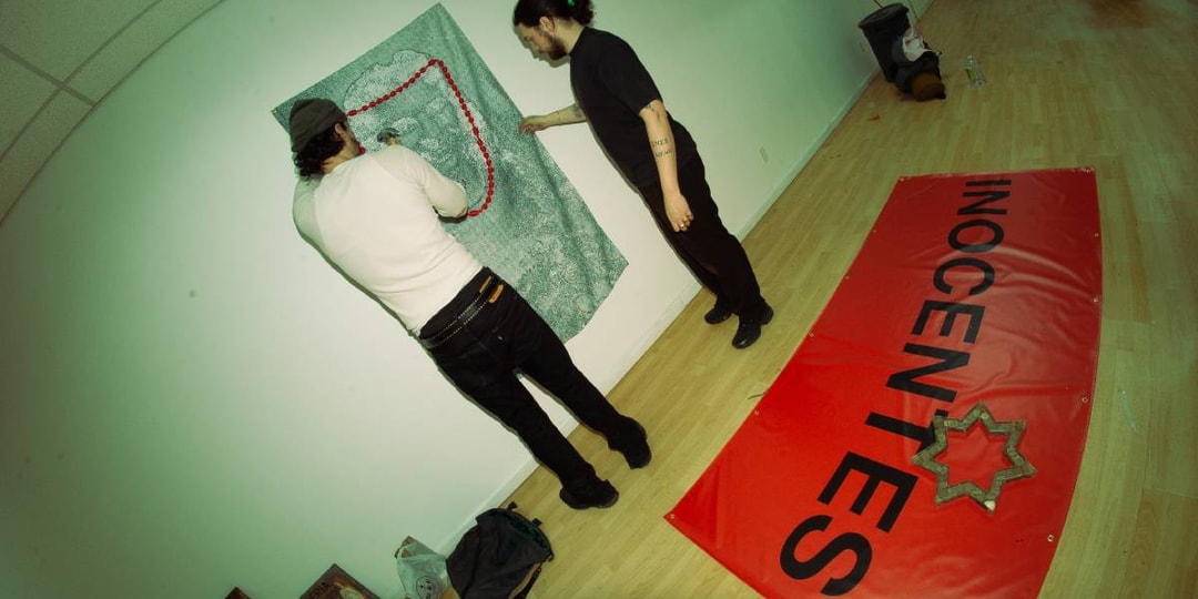 Deux personnes accrochent de l'art avec une bannière rouge au sol.