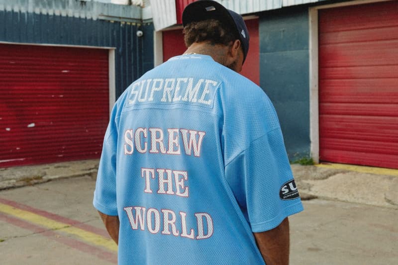 Personne portant un maillot bleu avec texte blanc dans une rue urbaine.