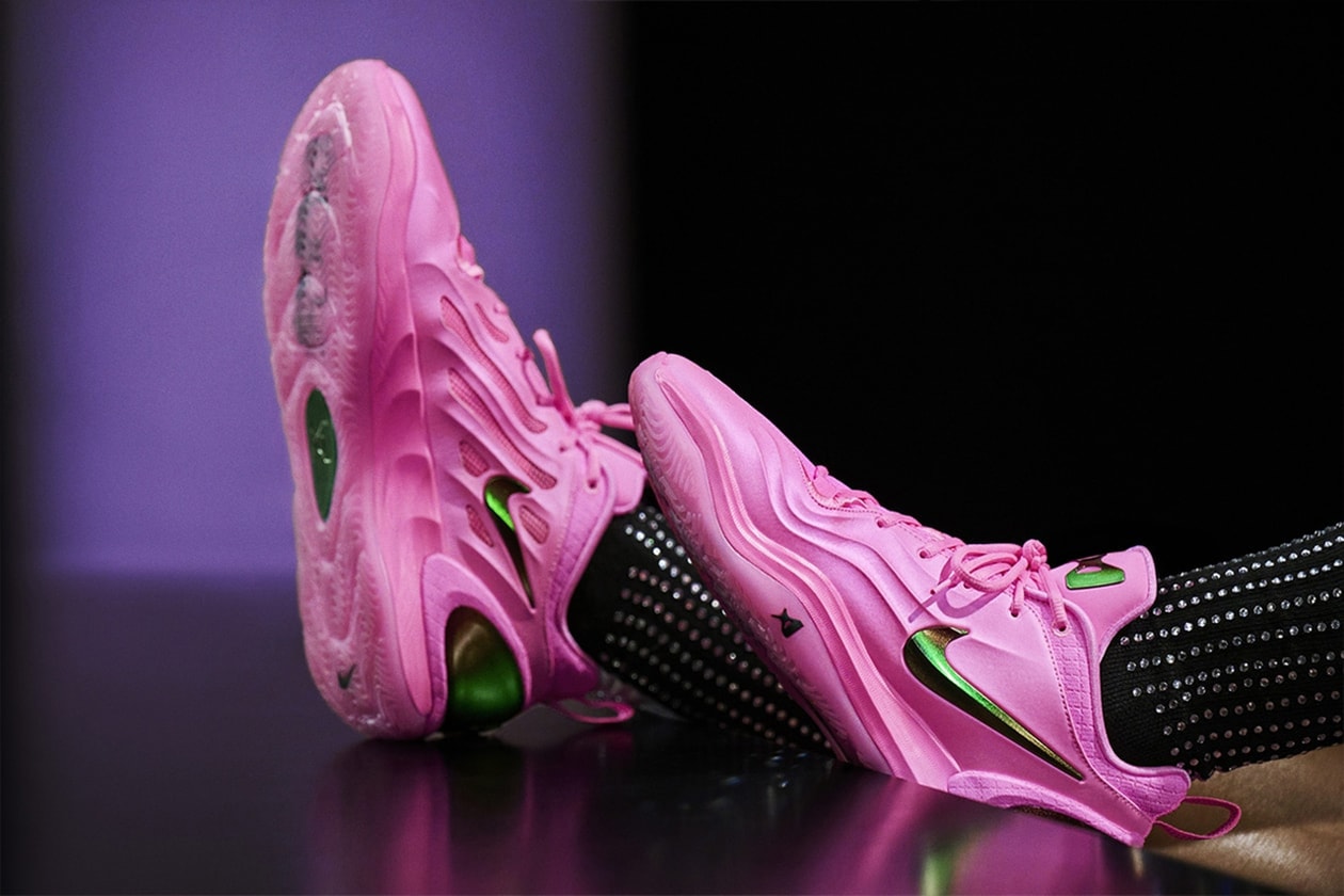 Chaussures de sport roses avec détails verts et noirs, portées sur fond sombre.