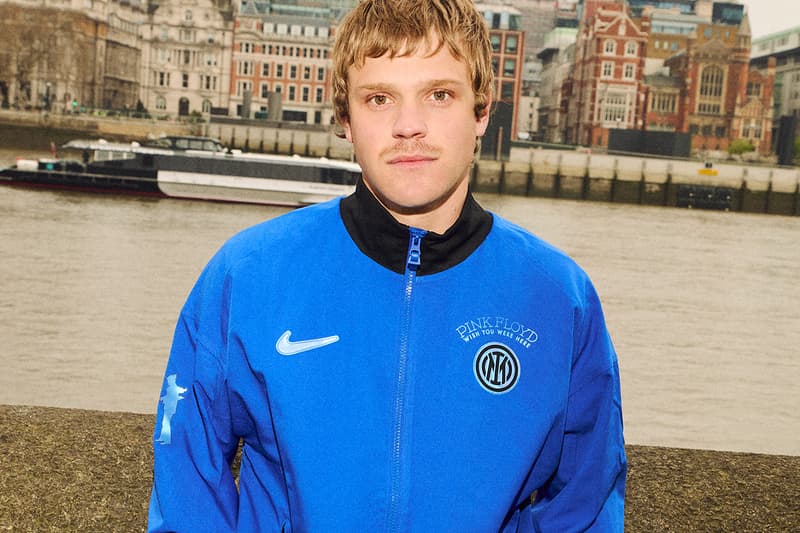 Homme en veste bleue devant une rivière en ville.