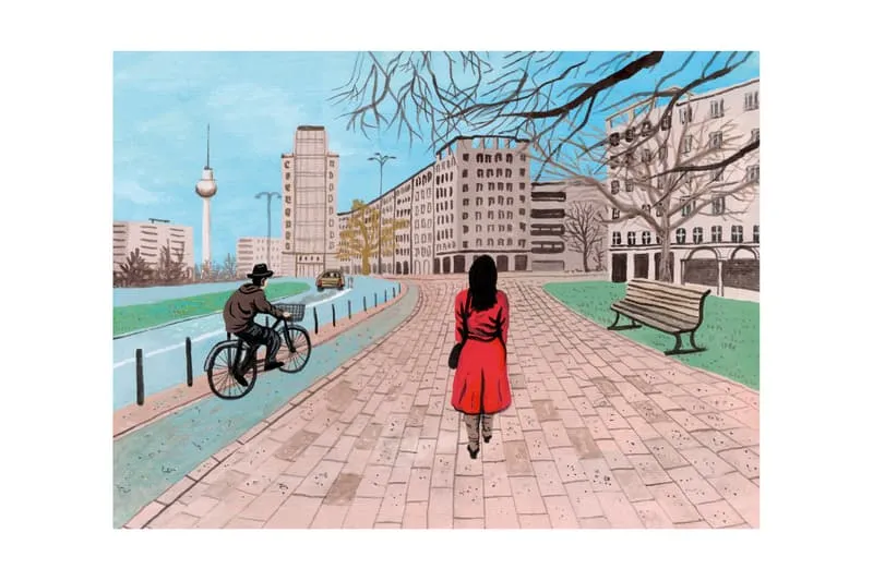 Femme en rouge sur chemin pavé, cycliste et bâtiments en arrière-plan.