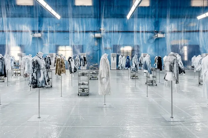 Exposition de manteaux artistiques dans une salle bleue transparente.