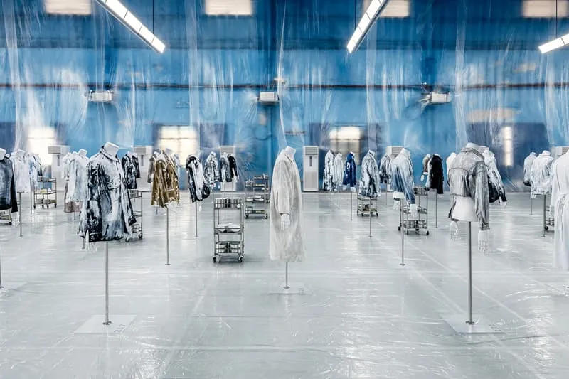 Exposition de manteaux suspendus dans une pièce bleue et transparente.