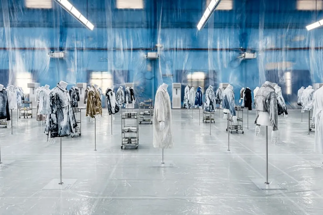 Exposition de manteaux artistiques dans une salle bleue transparente.