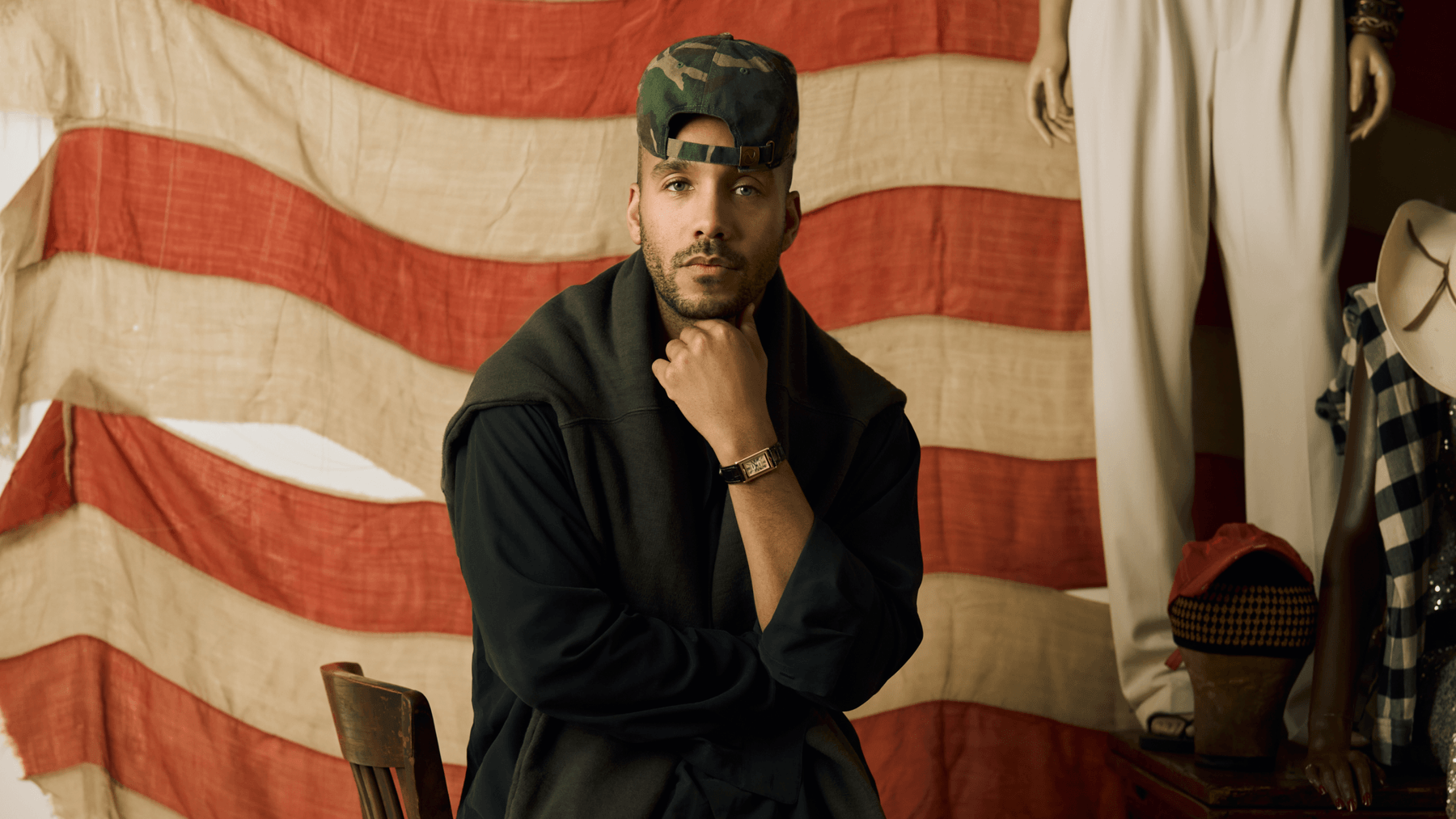 Homme assis devant un drapeau à rayures, portant une casquette camouflage.