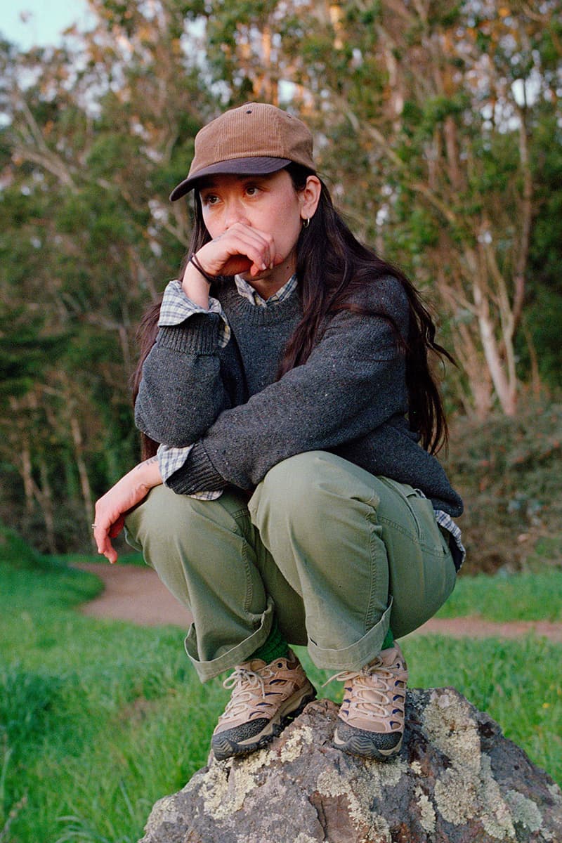 Personne accroupie sur un rocher en extérieur, avec casquette et vêtements décontractés.