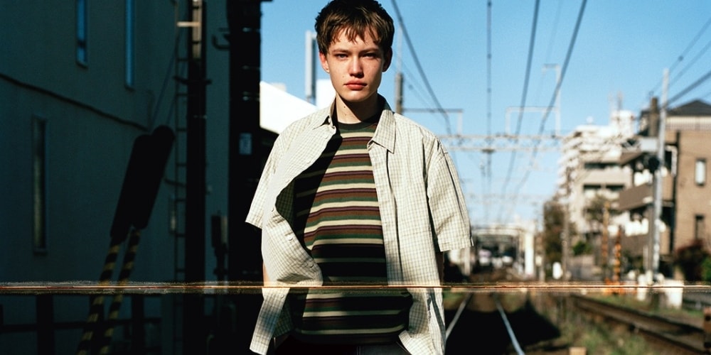 Personne devant une voie ferrée urbaine, portant une chemise à carreaux.