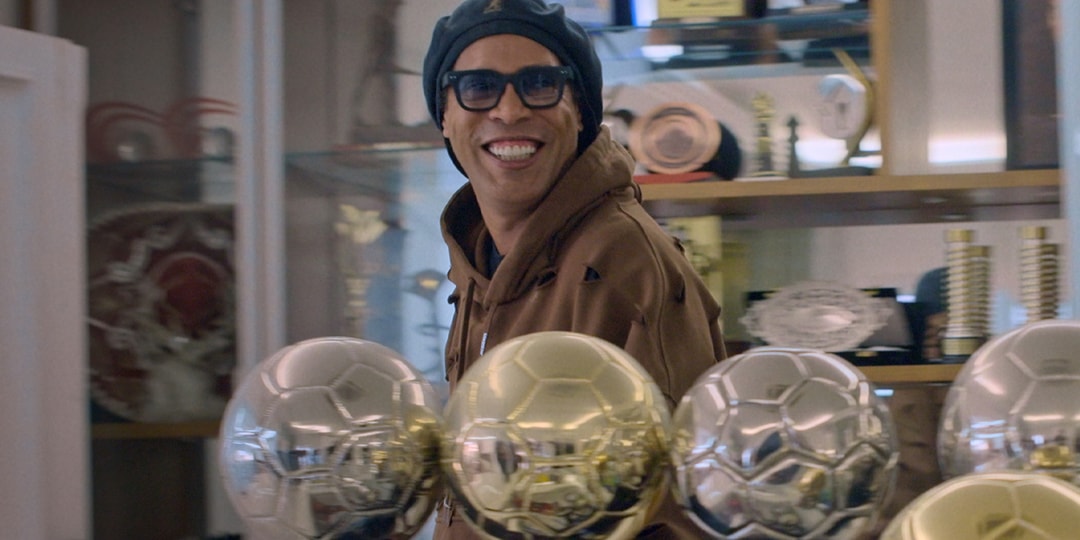 Homme souriant avec des trophées dorés en arrière-plan.